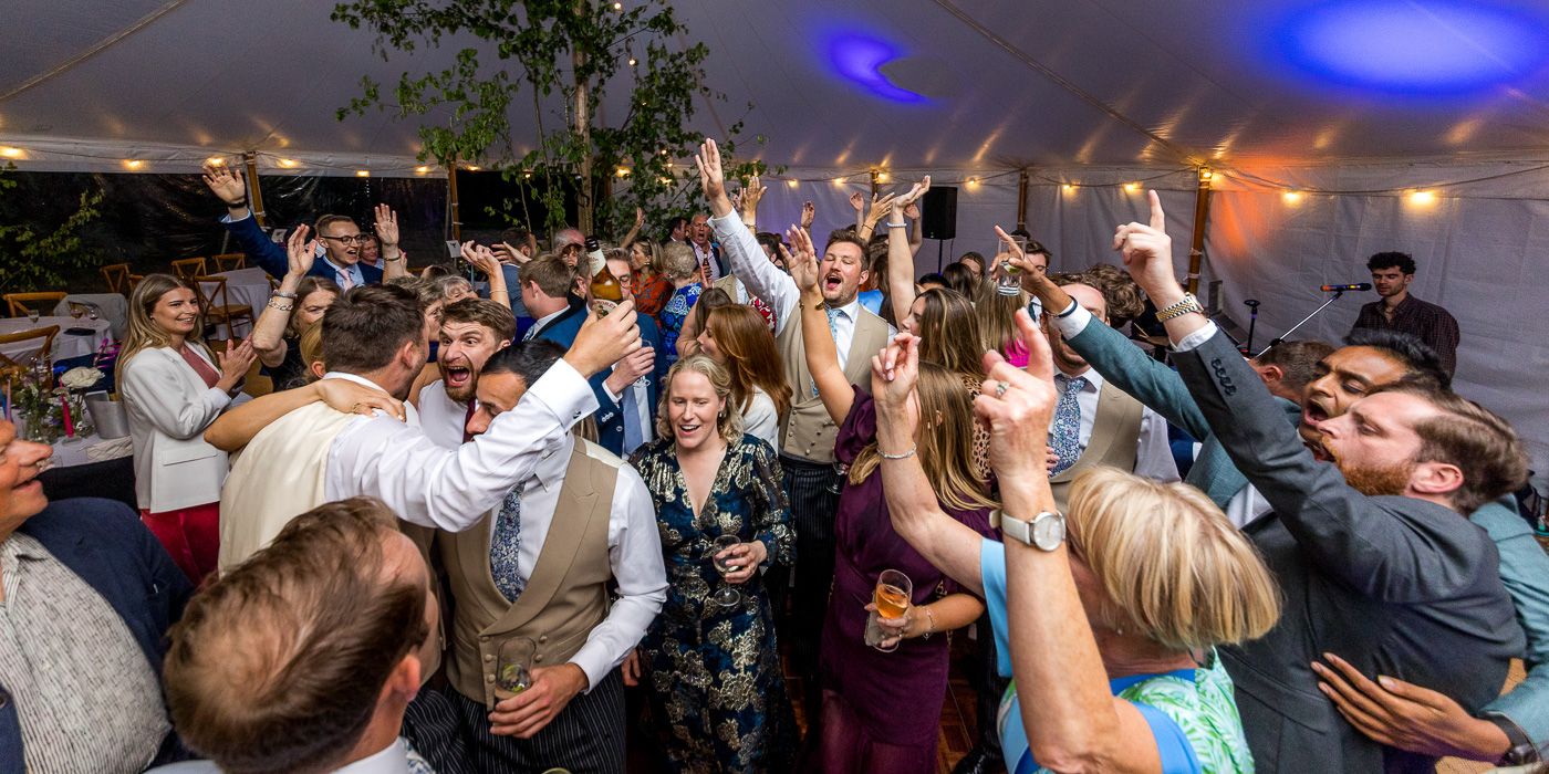 Wedding reception dance floor filled with guests celebrating under blue and orange lights.