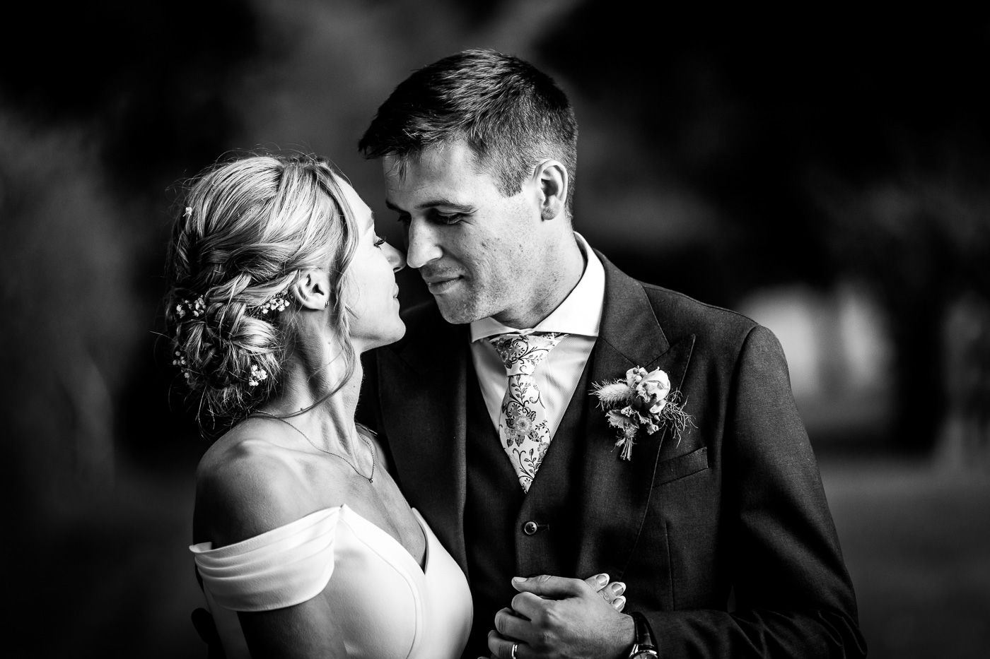 A romantic black and white wedding portrait of a couple sharing an intimate moment outdoors.