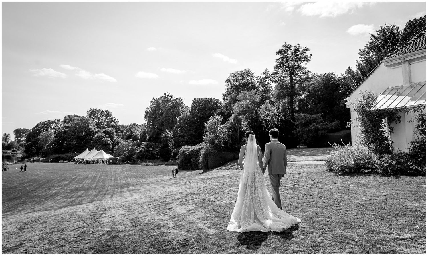 A black and white wedding photo showing a couple walking on a grassy lawn near a white building.