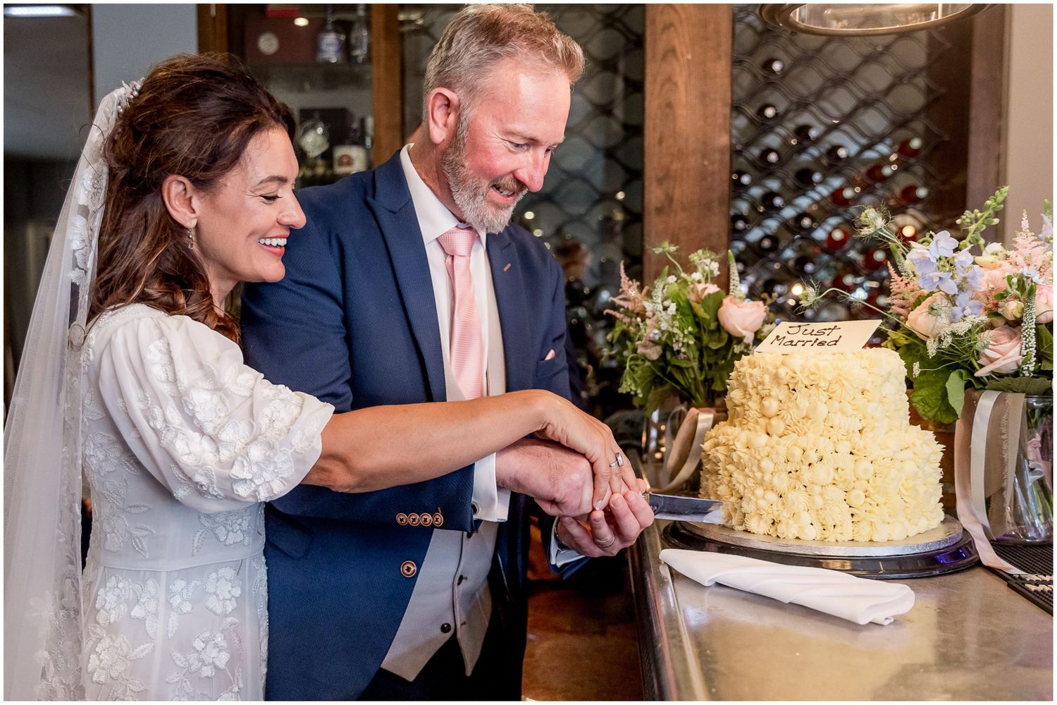 Wedding cake cutting ceremony with a white tiered cake decorated with flowers.