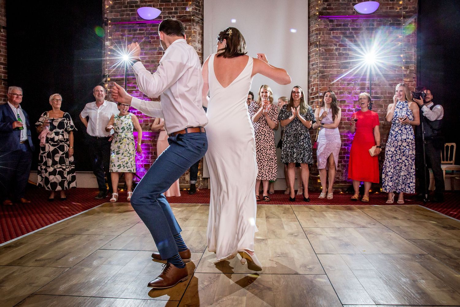 Dance floor action shots during wedding reception in rustic brick venue with colored lighting.