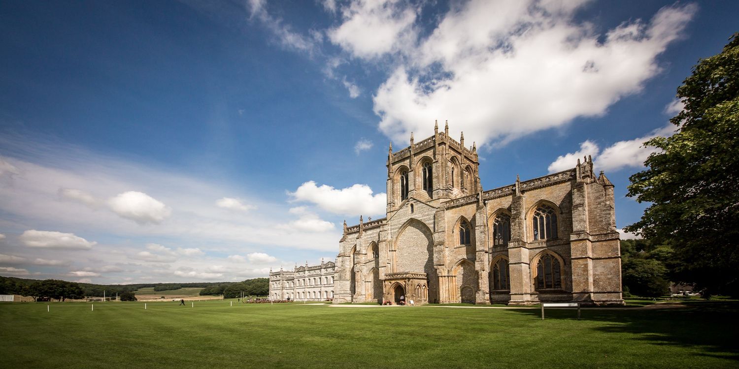 Panoramic view of a historic stone church and grounds under blue summer skies.