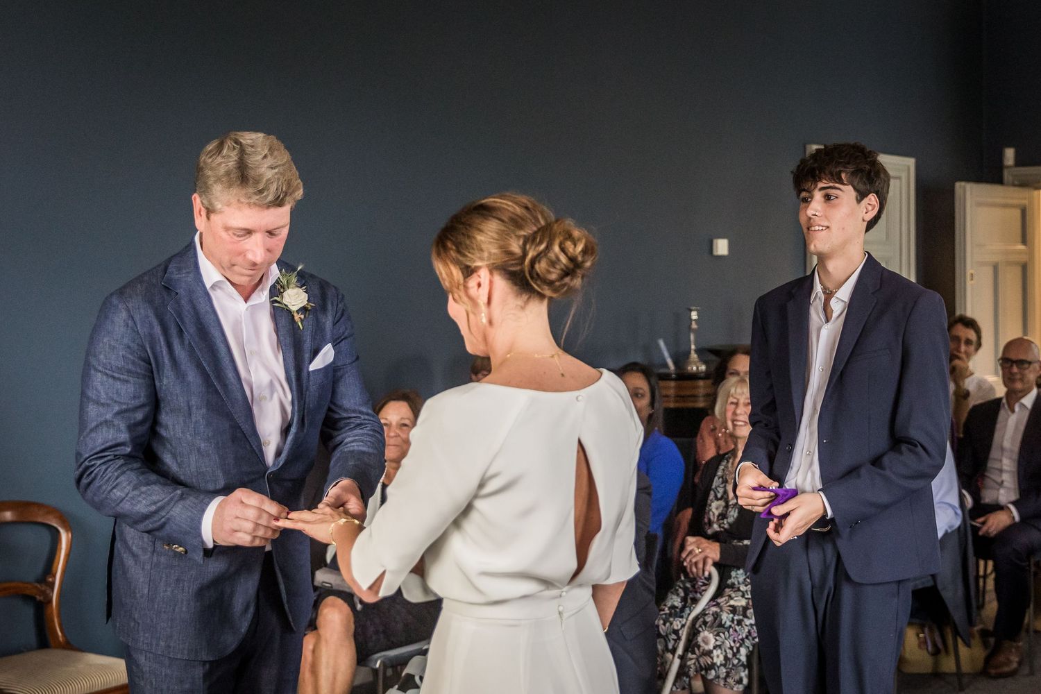 A wedding ceremony moment captured in a room with navy blue walls and natural light.