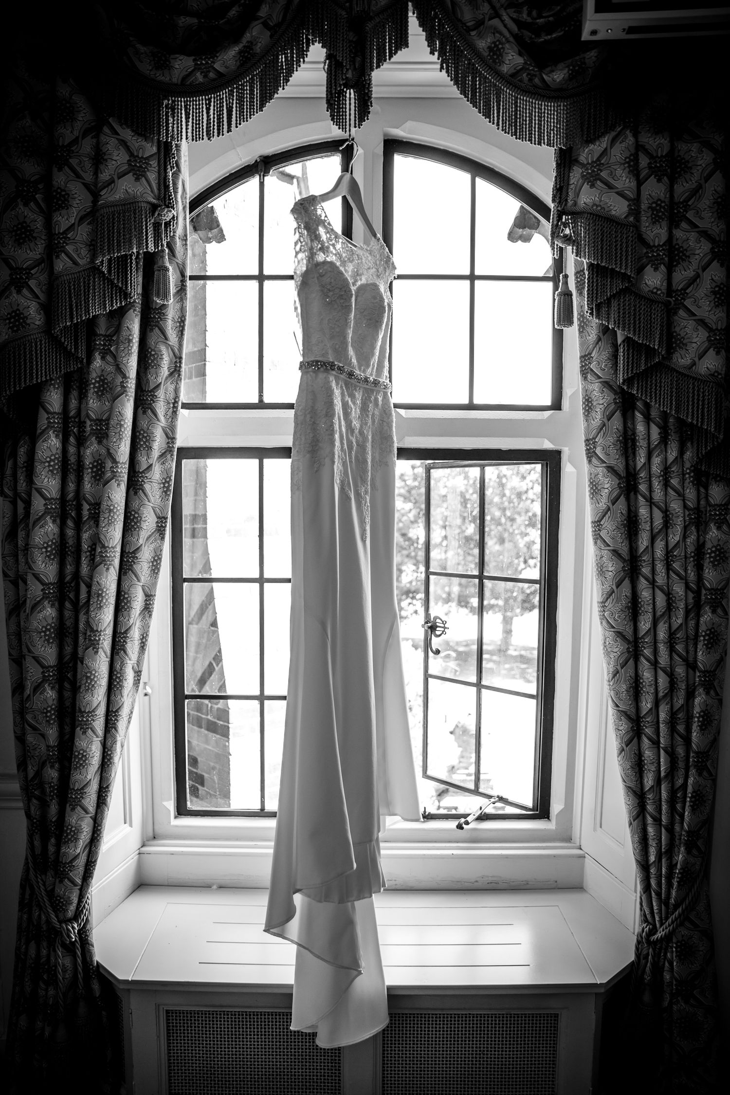 Black and white photo series of a white wedding dress hanging in arched windows.