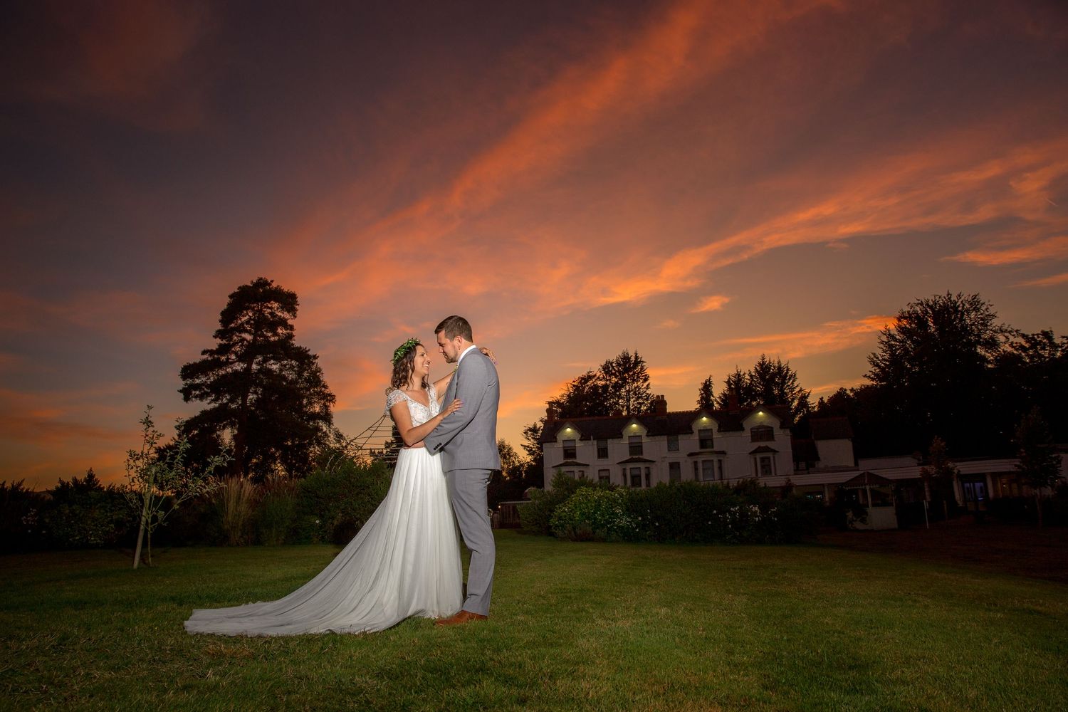 Romantic sunset portrait of newlyweds against dramatic orange sky.