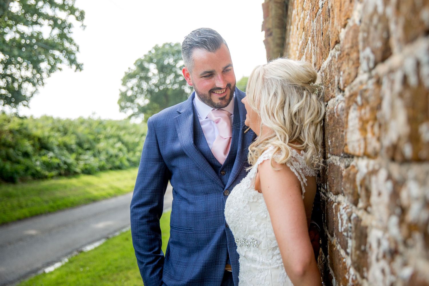 Couple shares intimate moment against rustic stone wall in elegant wedding attire.