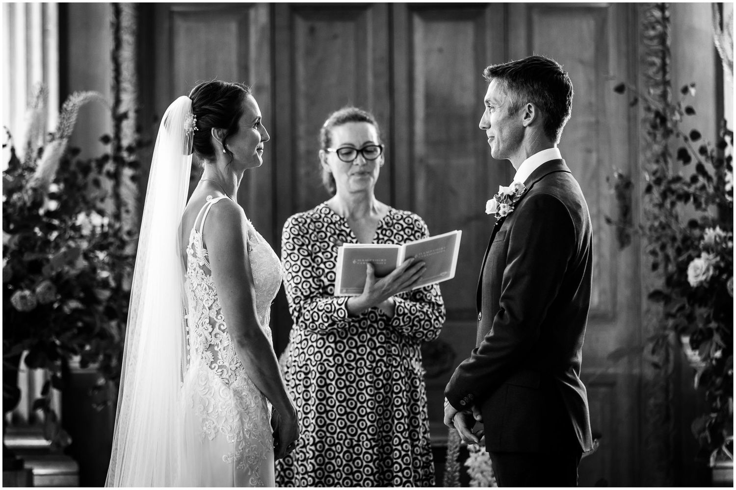 The bride, wearing a veil, turns to face the groom as they make their wedding vows at Walhamton School near Lymington.