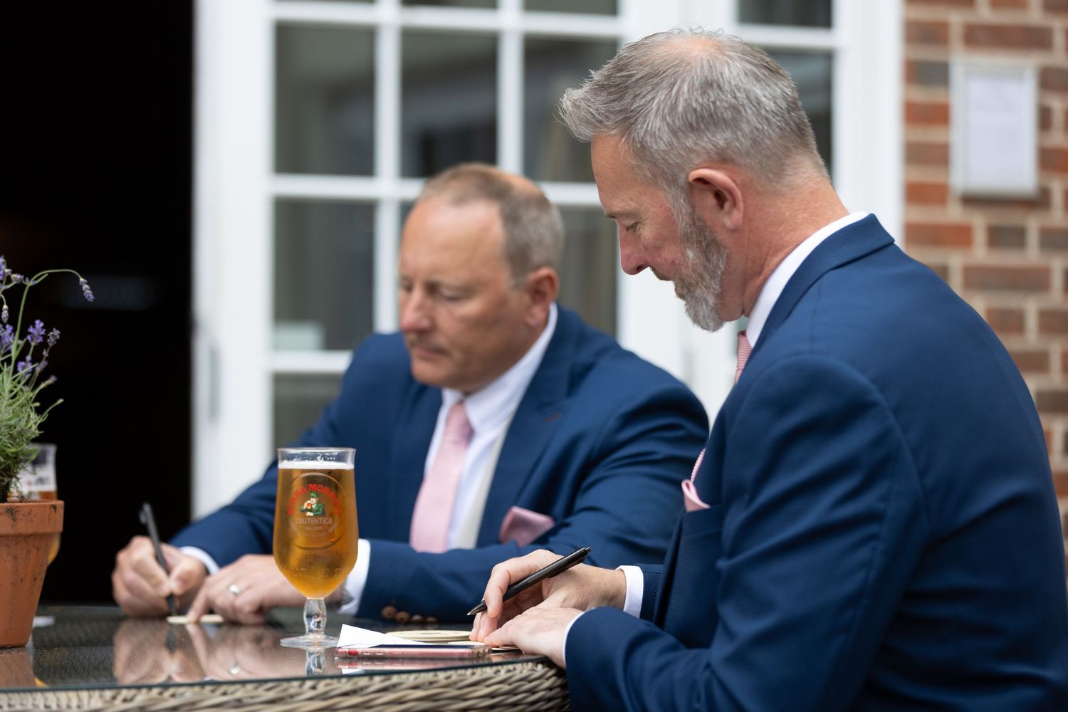 Two men in blue suits sitting at an outdoor table with drinks.