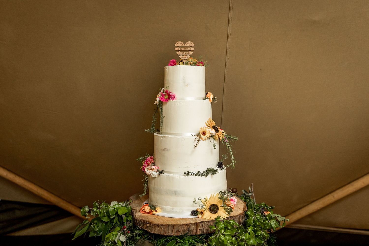 Elegant white wedding cake decorated with fresh flowers and greenery on a rustic stand.