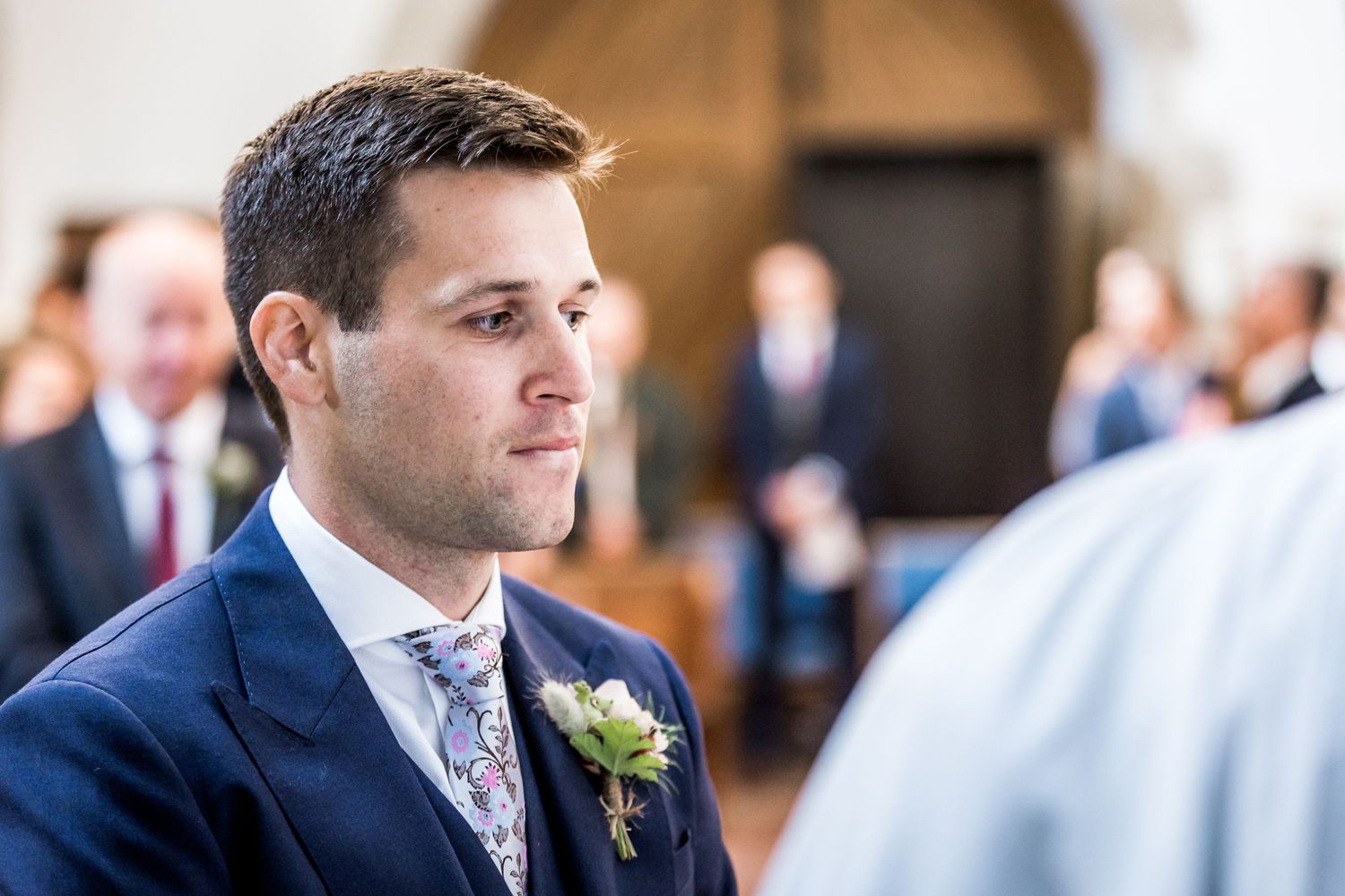 Wedding ceremony attendees in formal attire inside traditional church interior.