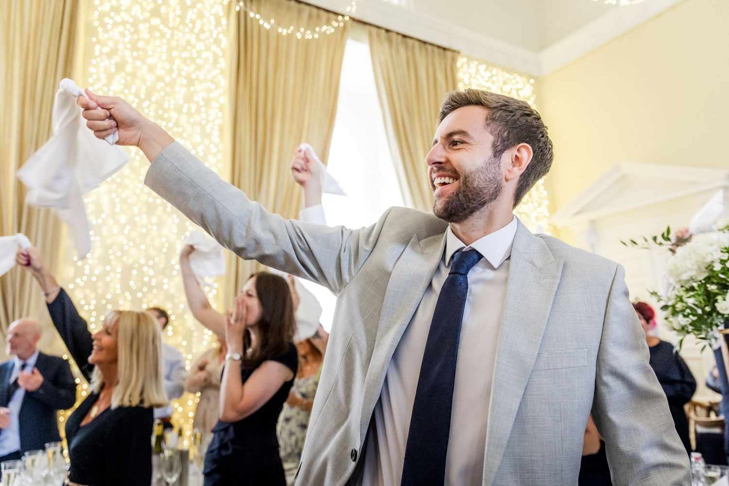 Wedding guests celebrating with raised arms in formal reception hall.