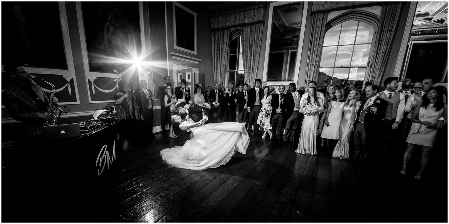 Black and white photo of a couple sharing their first dance at a wedding reception with guests watching in an elegant ballroom.
