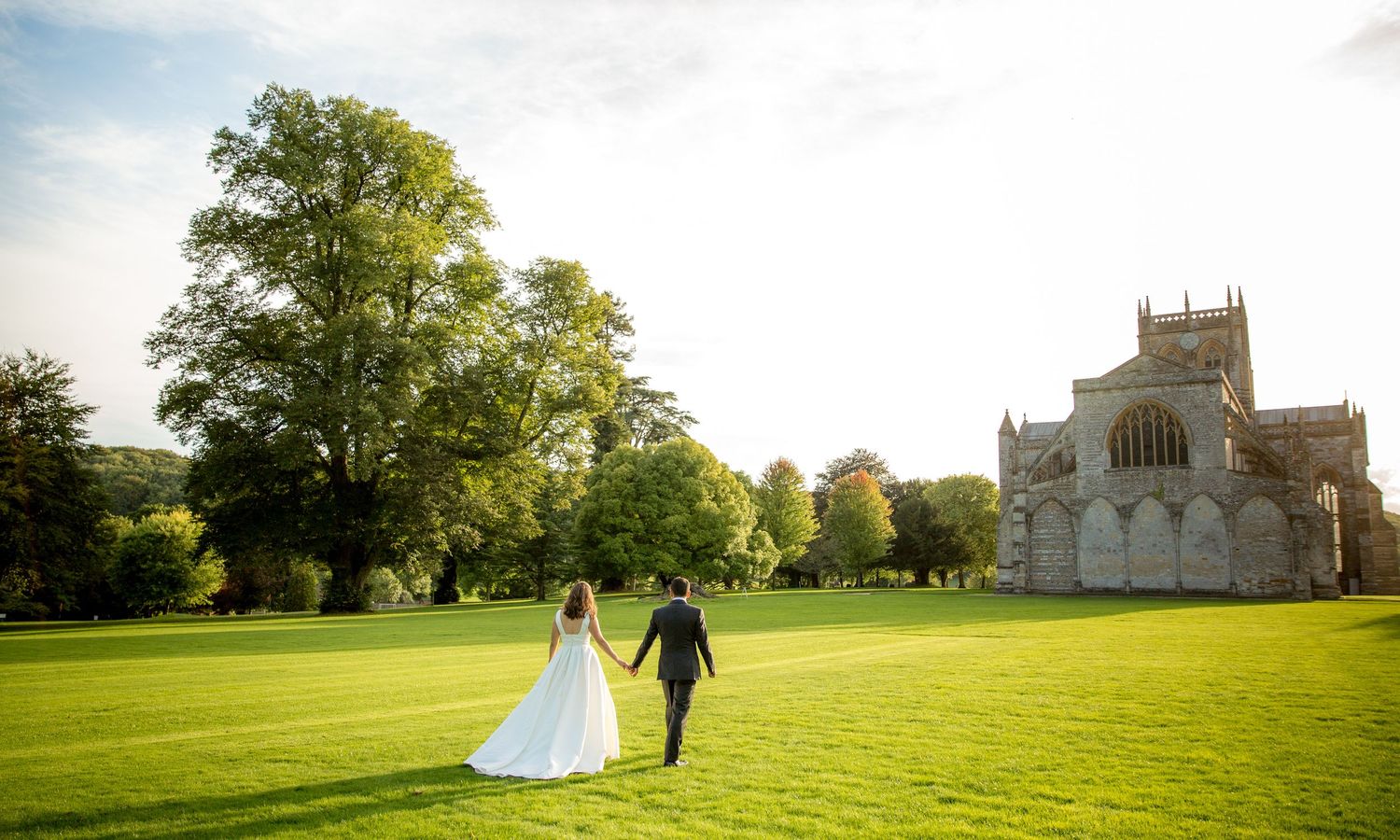 Newlyweds walking across sprawling green lawns with a grand chapel in the background.