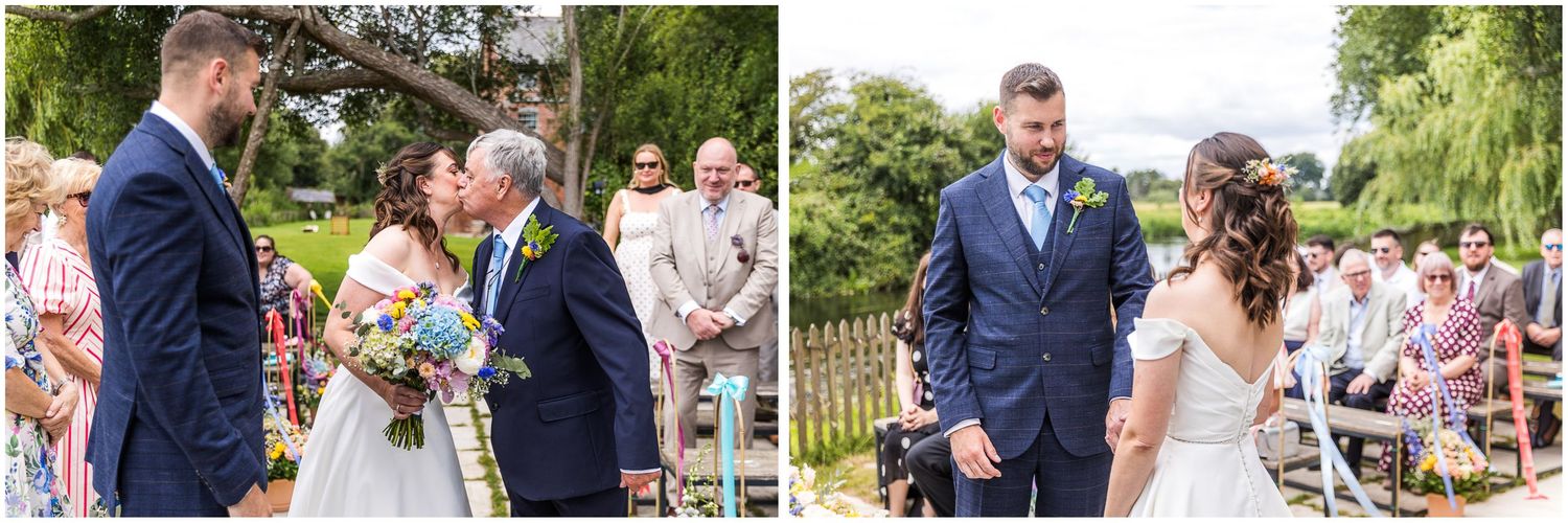 Bride and groom share a kiss at an outdoor wedding ceremony with guests seated on wooden benches in a garden setting.