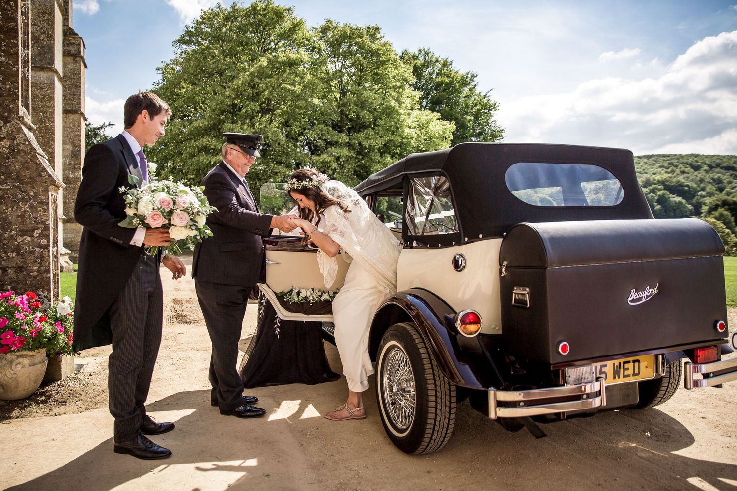 Classic vintage wedding car parked outside a historic stone building.