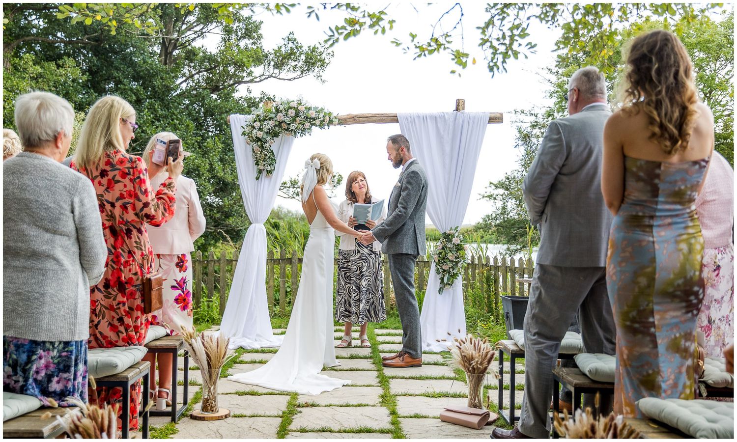 Wedding ceremony setup with white arch and guests seated along stone pathway.