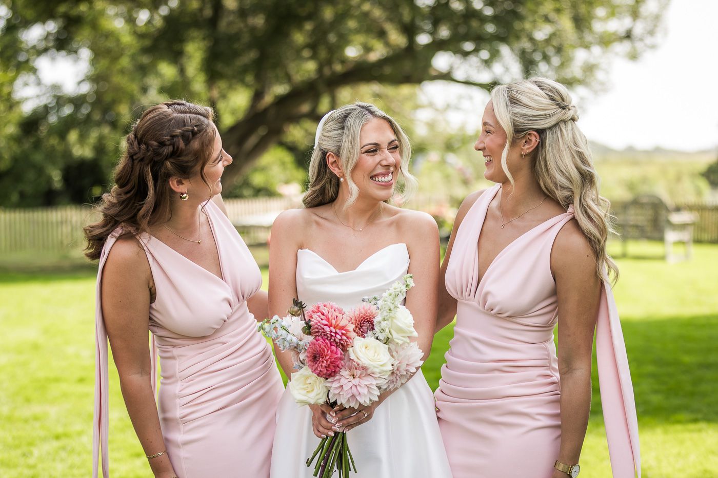 Bridesmaids in pink dresses sharing candid moments outdoors.