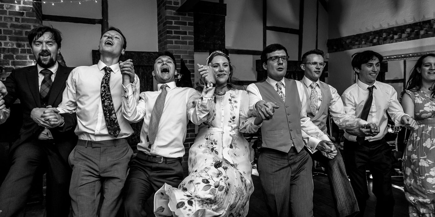 Black and white photo of groomsmen lined up against brick wall.