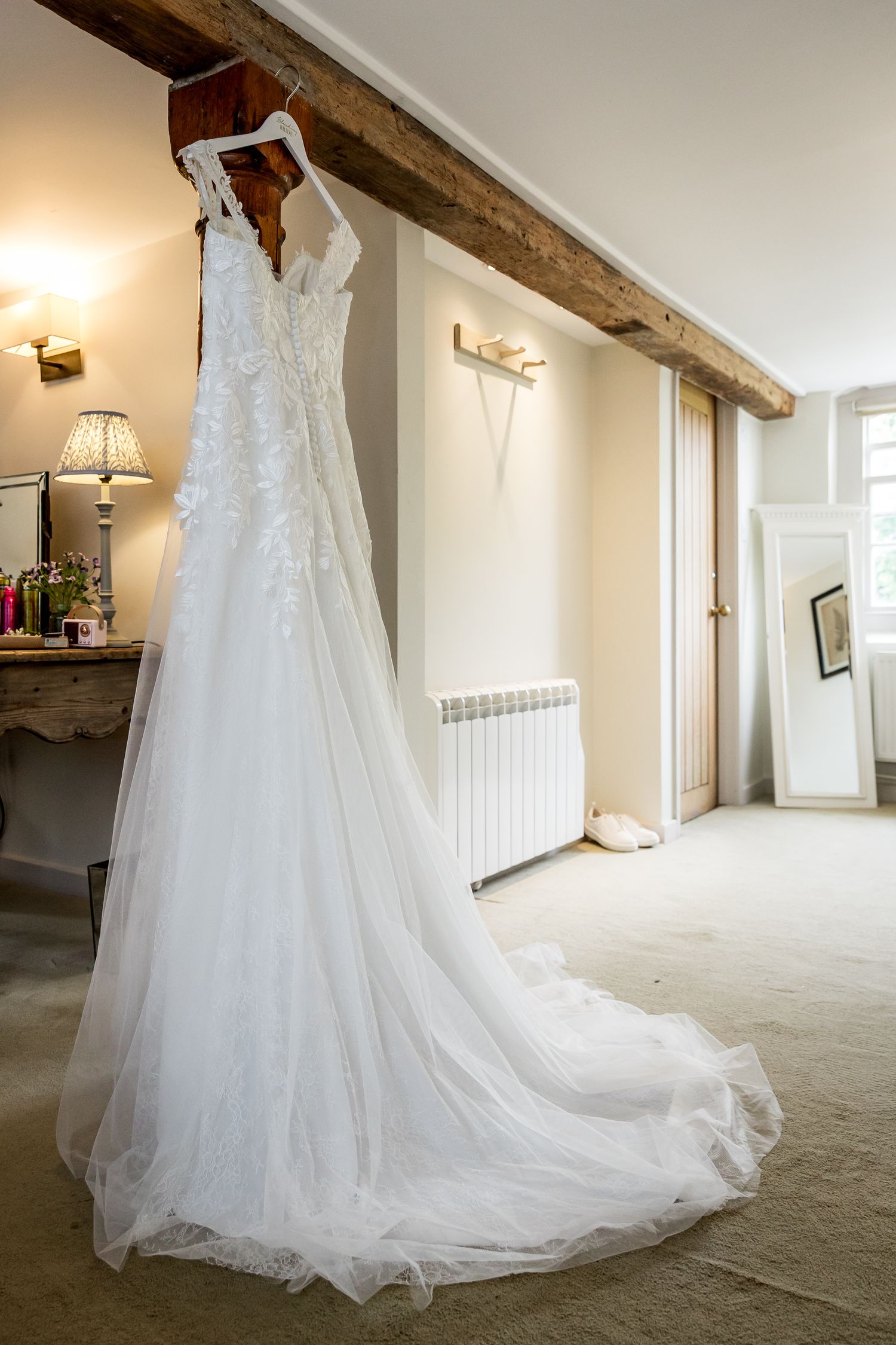 Elegant white wedding dress with long train hanging in rustic venue with exposed wooden beams.