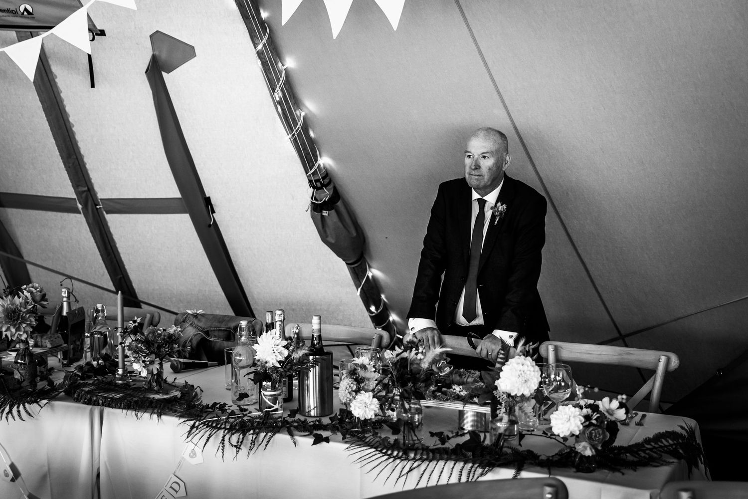 Wedding reception in a large tent with guests seated at long tables for dinner service.