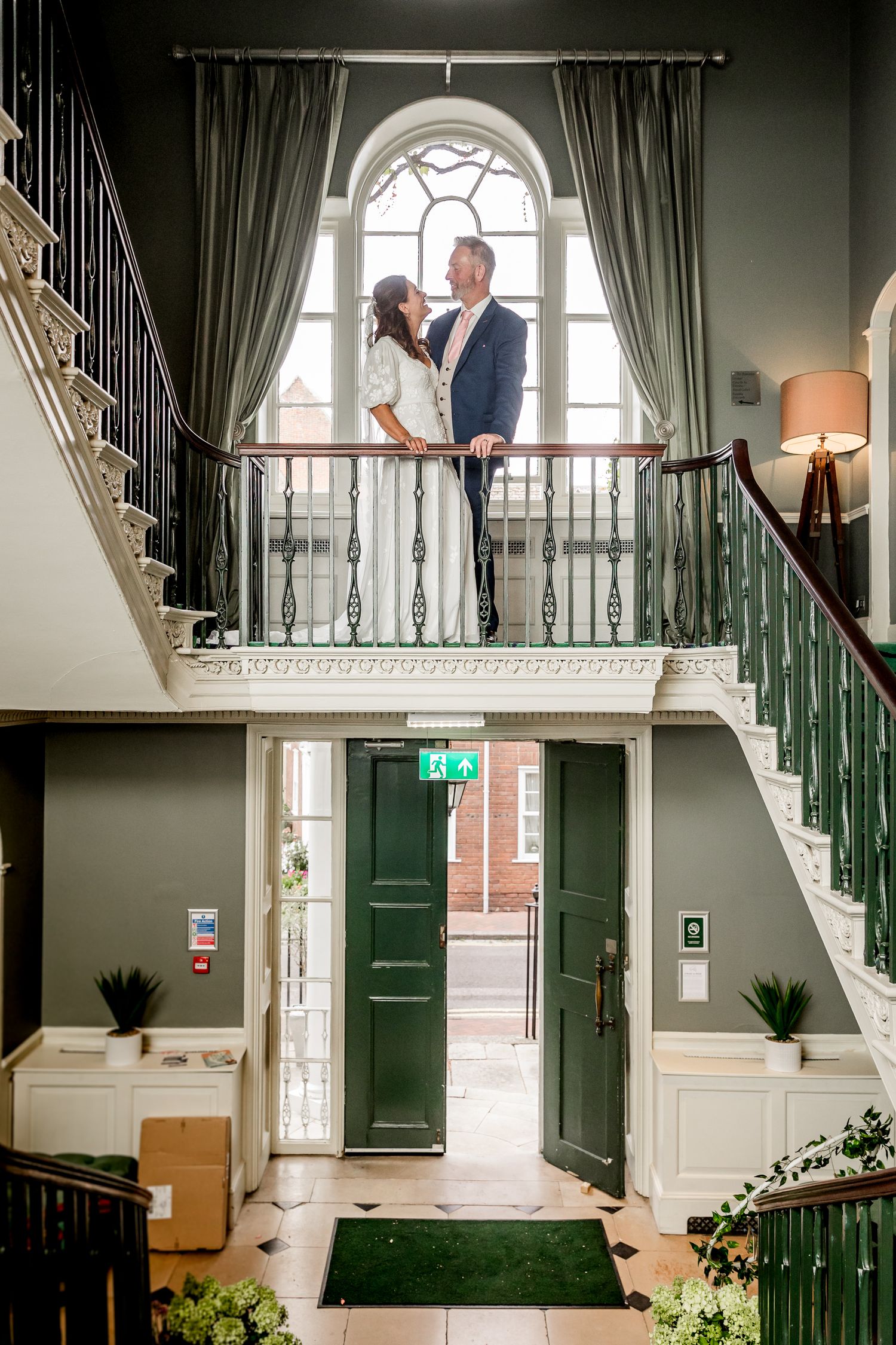 Elegant interior staircase with green doors and natural light streaming through arched windows.