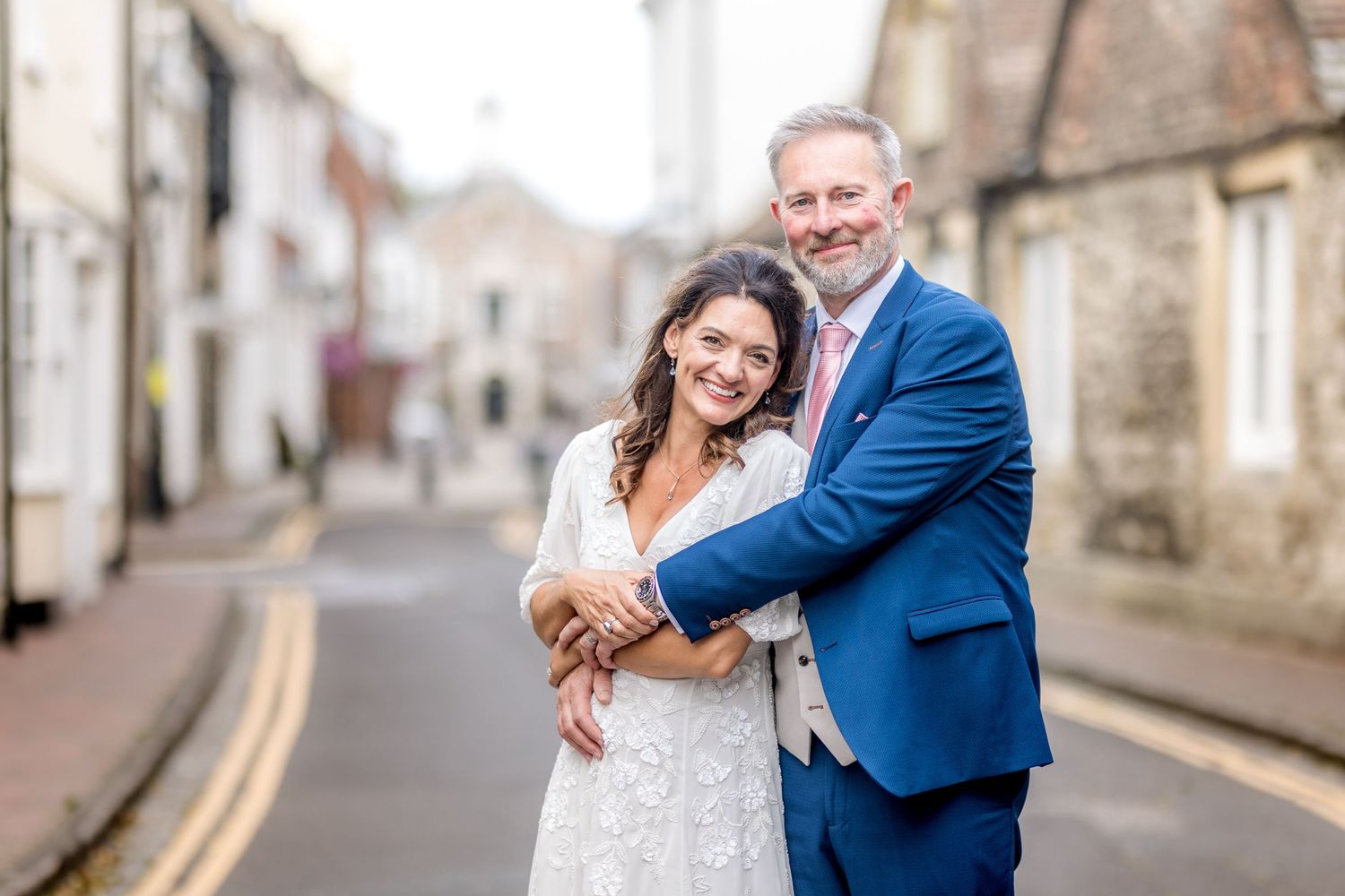 A couple shares an intimate moment on a quaint village street with traditional stone buildings.