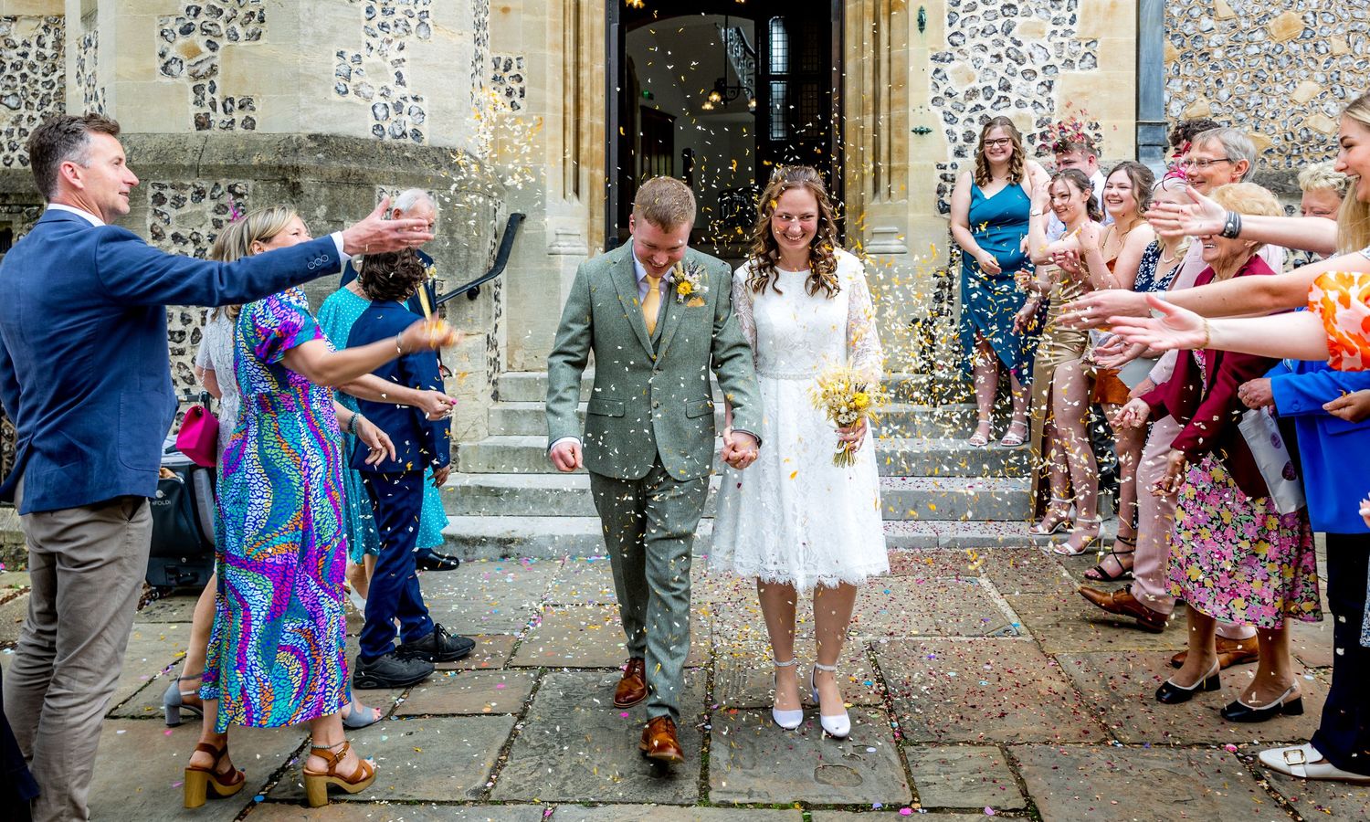 Wedding guests celebrating and throwing confetti outside a historic church.
