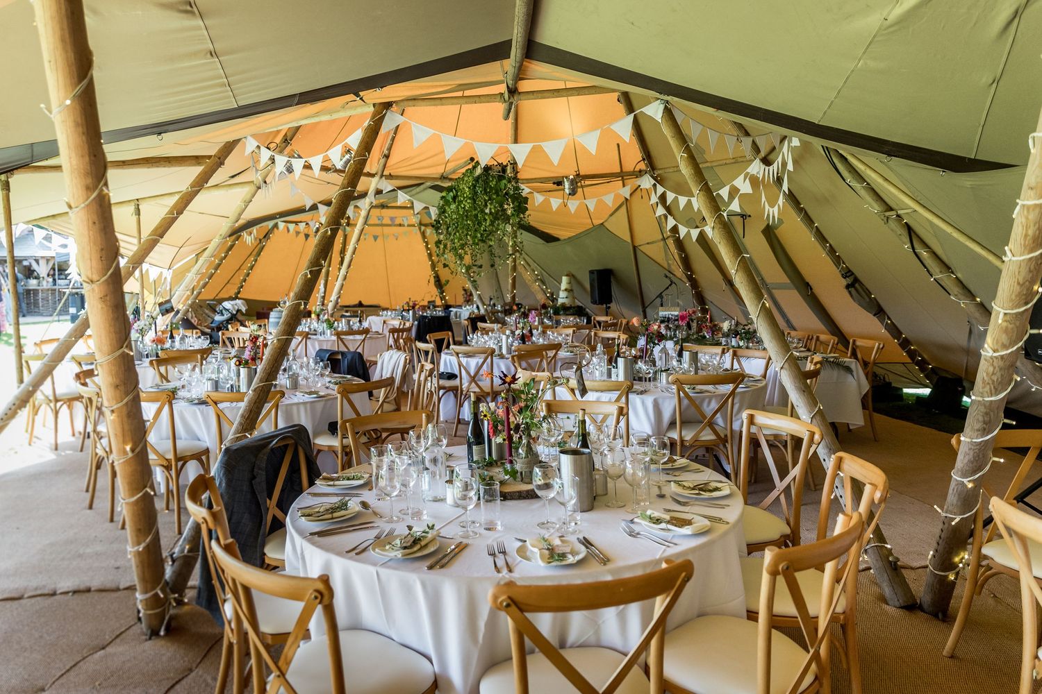 Interior of a large tipi wedding venue with round tables and rustic decorations.