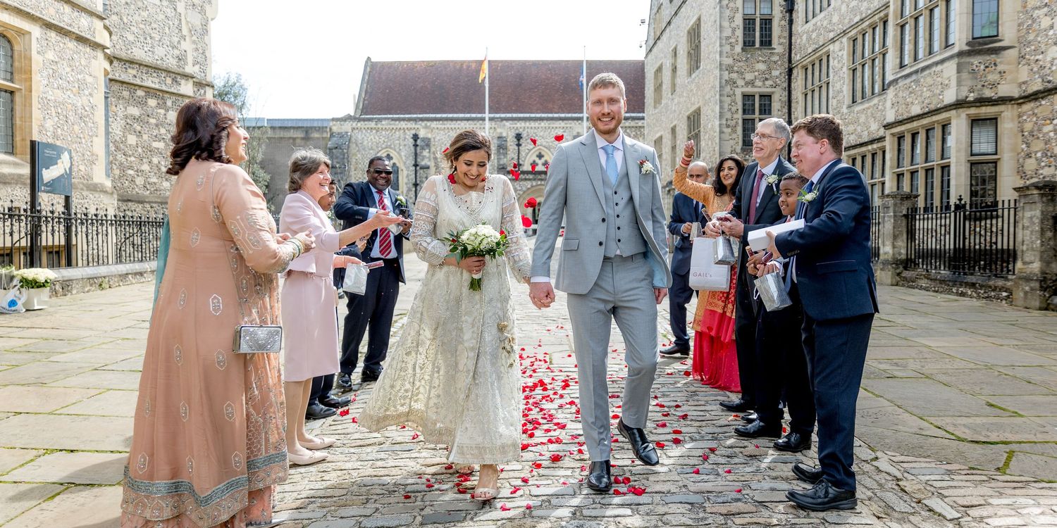 Wedding guests line up outside a historic stone building to celebrate the newlyweds.