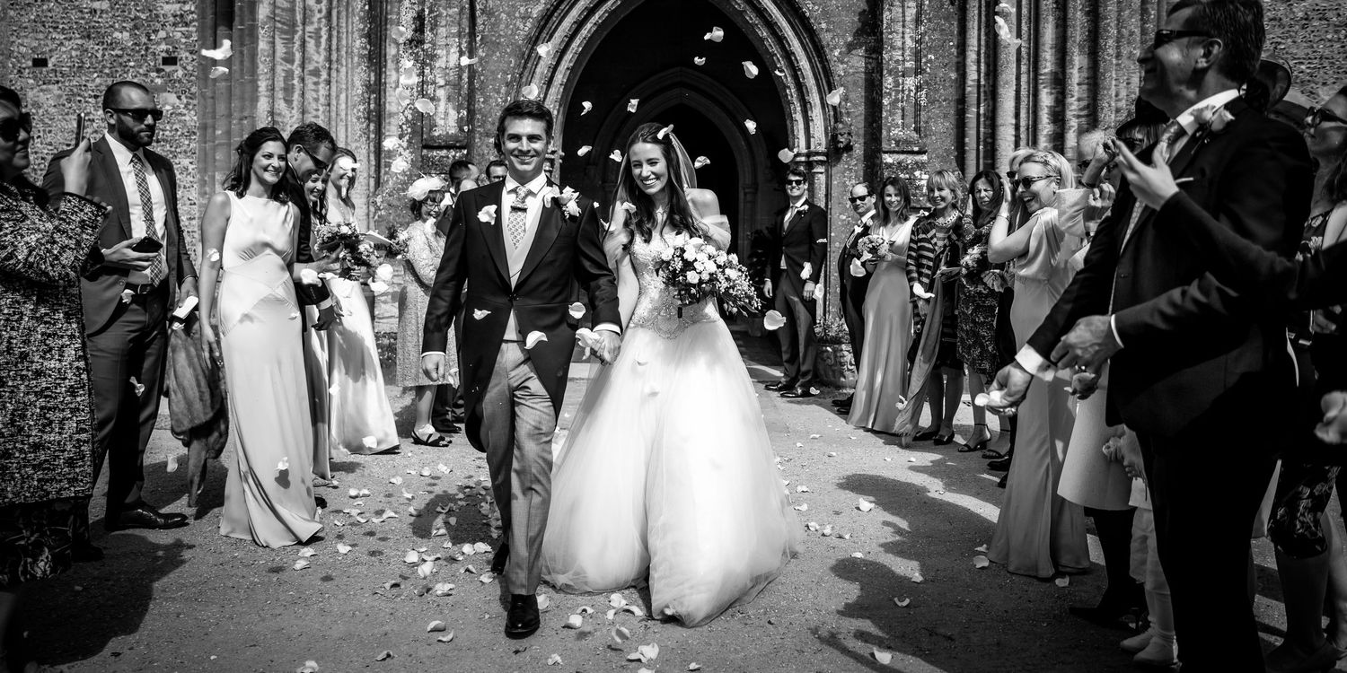 Wedding party and guests celebrating outside historic church with confetti.