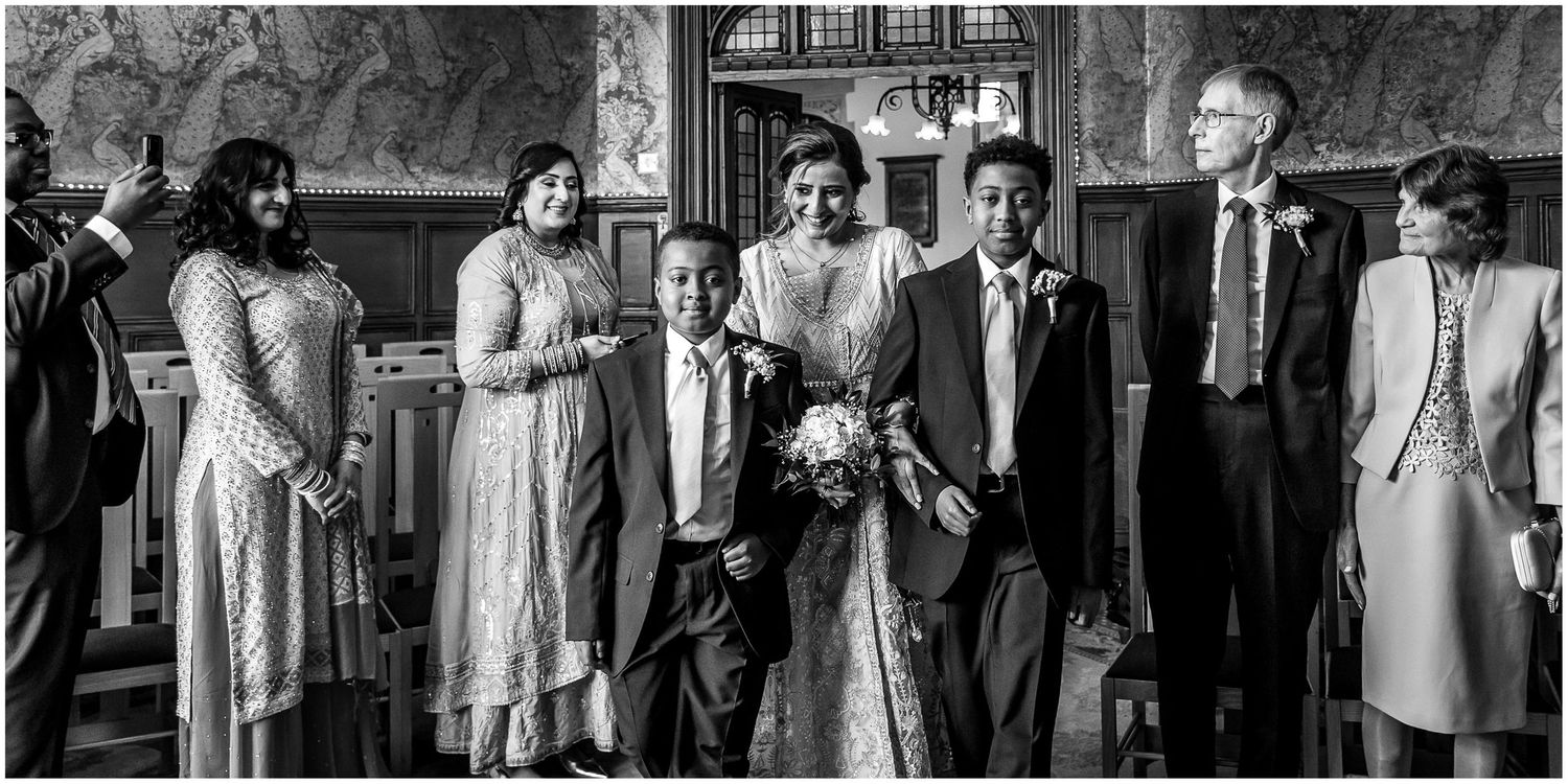 Black and white photo of wedding guests gathered in an ornate indoor space.
