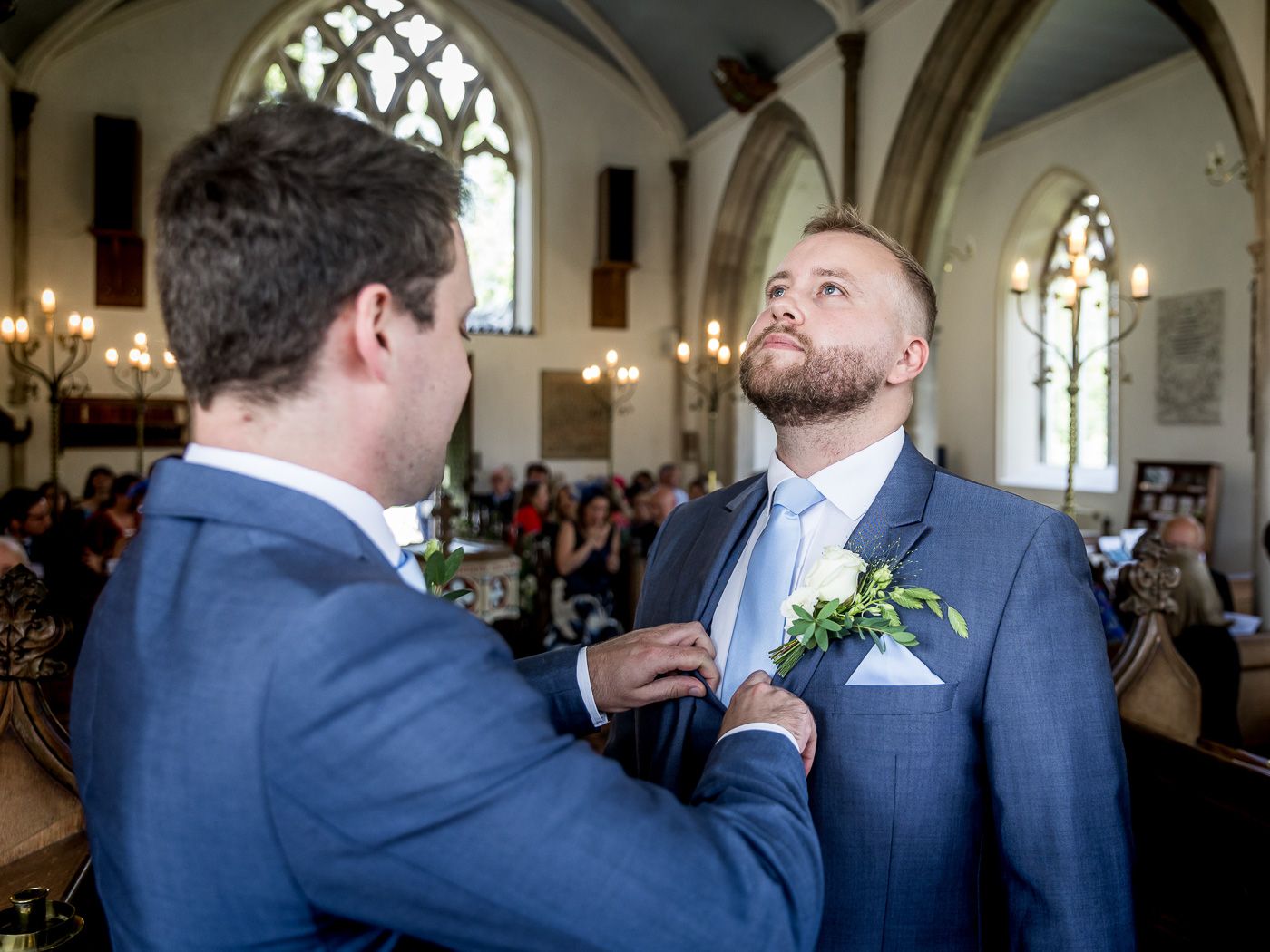 Wedding party in navy suits gathered inside a gothic church with stained glass windows.
