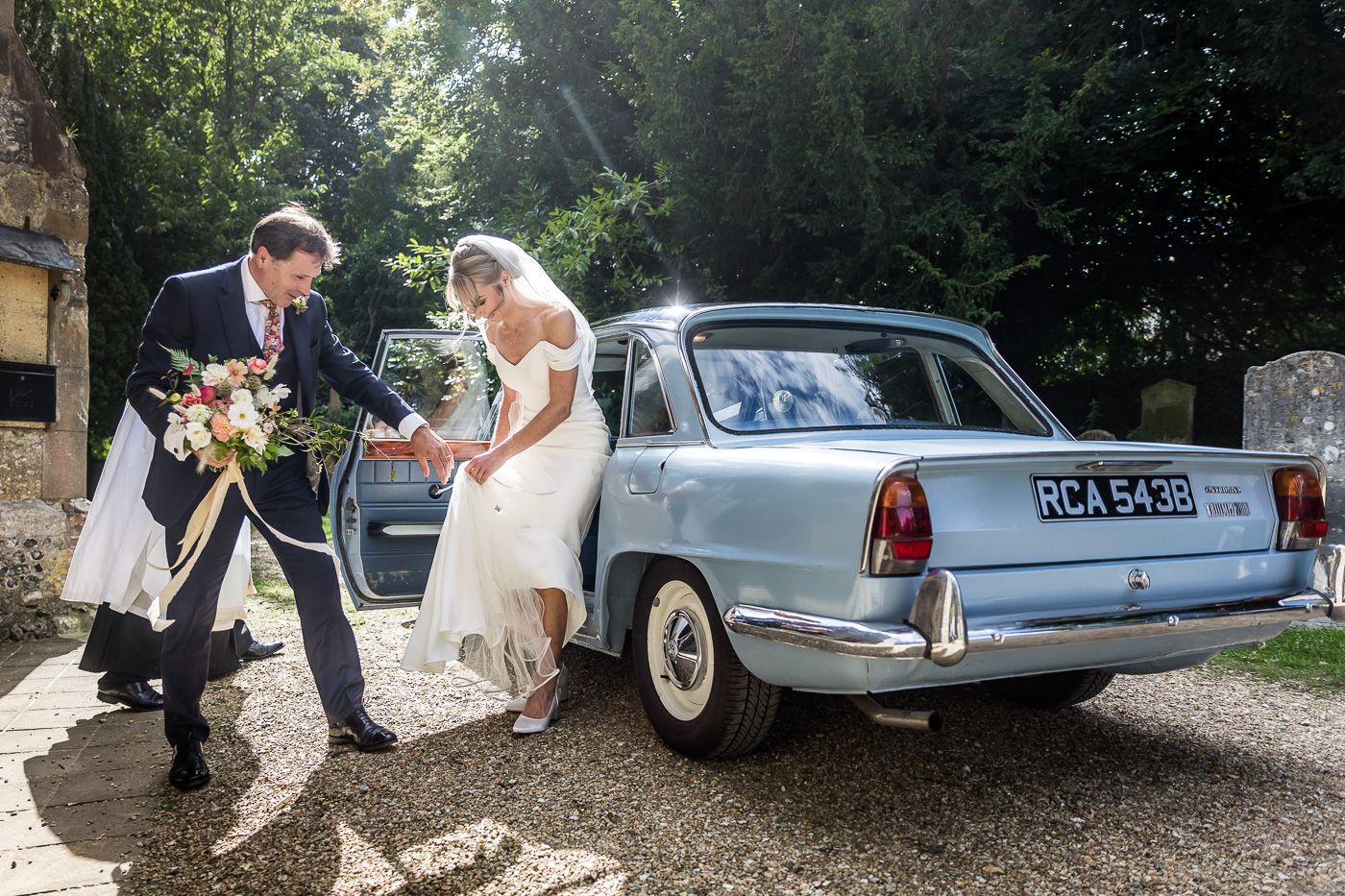 Classic vintage wedding cars parked along a tree-lined driveway.