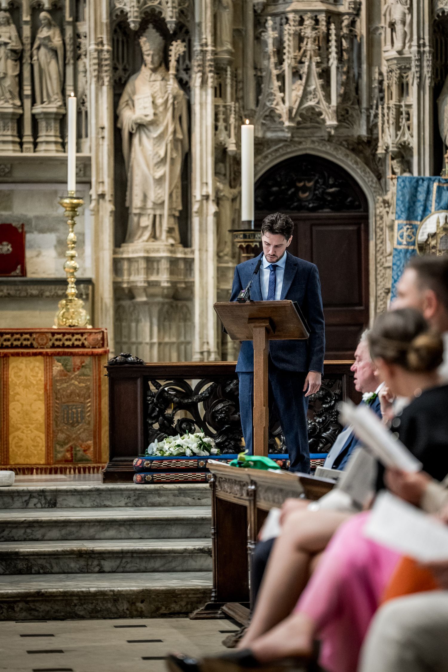 Church ceremony with ornate Gothic stone carvings and decorative wooden details in background.