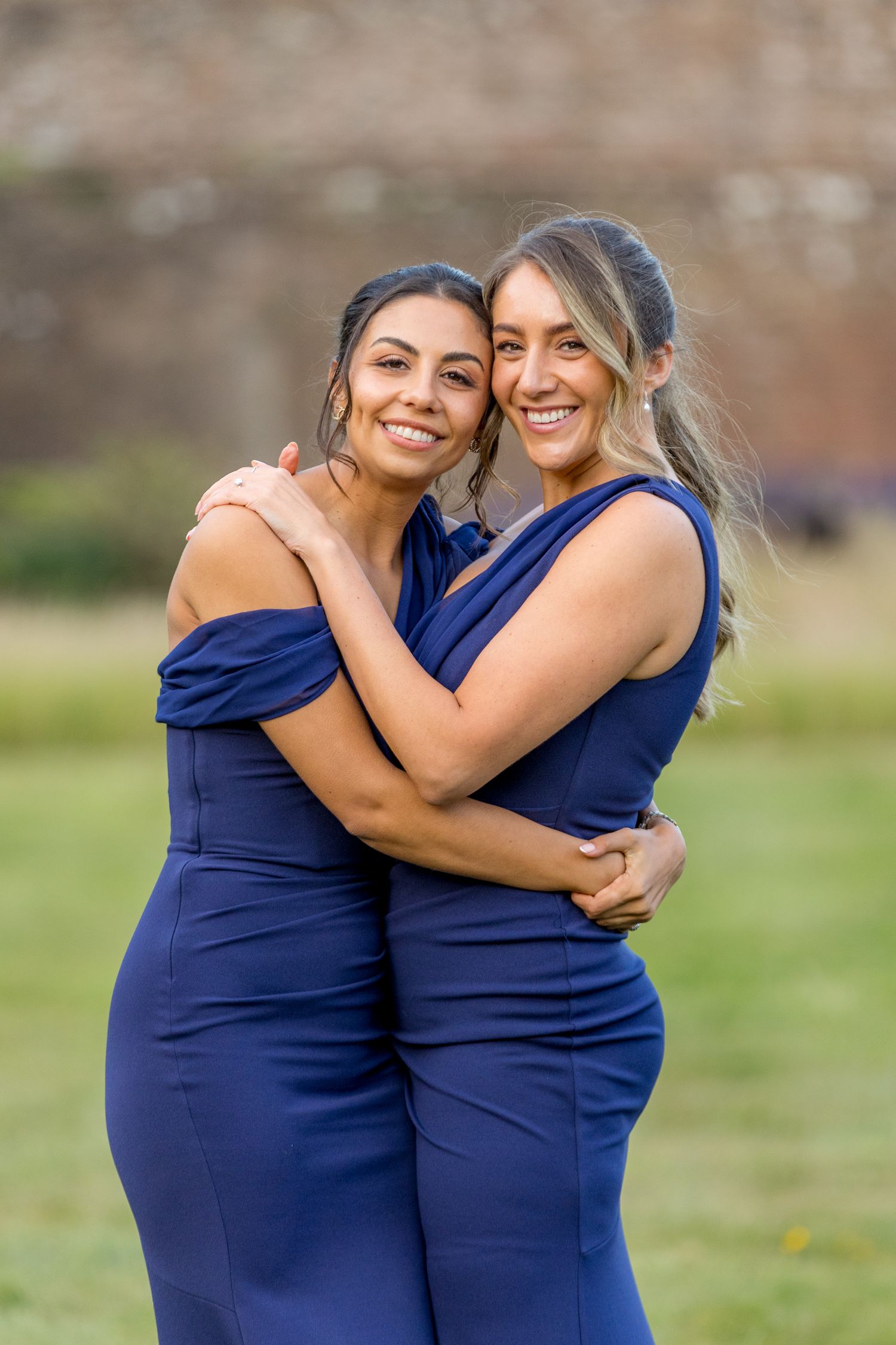 Bridesmaids in matching navy blue dresses embrace and laugh together outdoors.