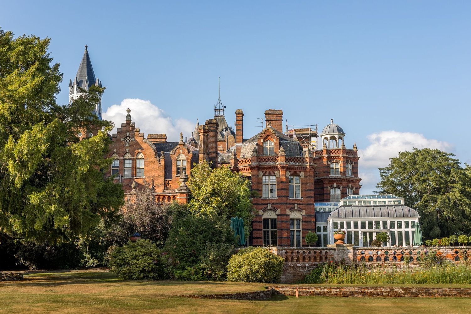 Panoramic view of a historic red brick mansion with ornate architecture and landscaped grounds on a sunny day.