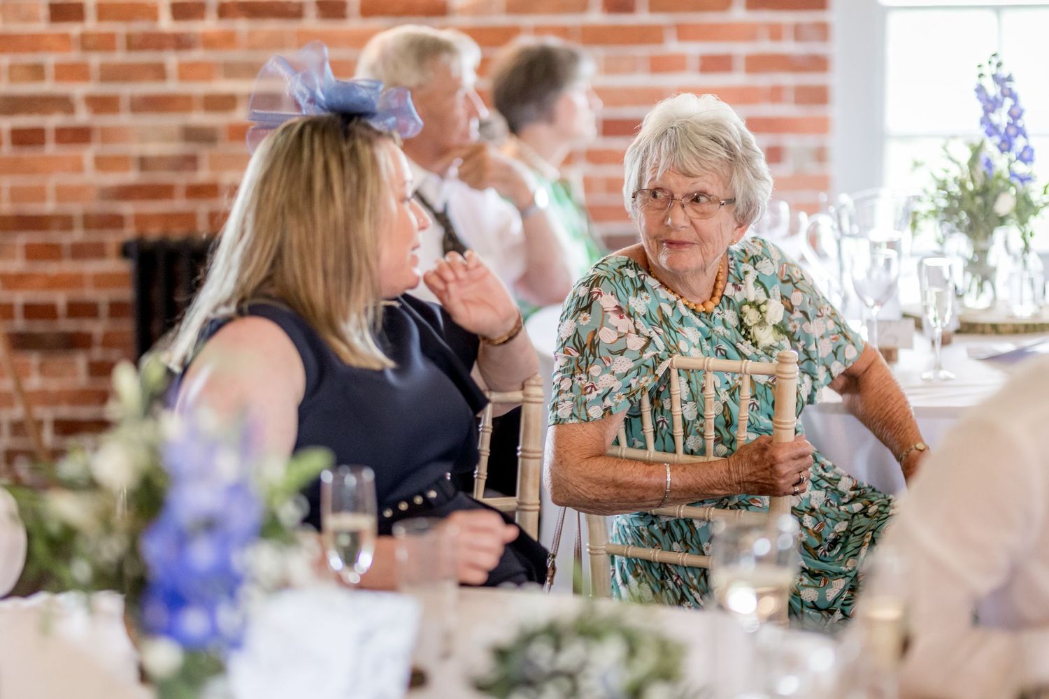 Wedding guests raising glasses during toasts at reception with floral centerpieces.