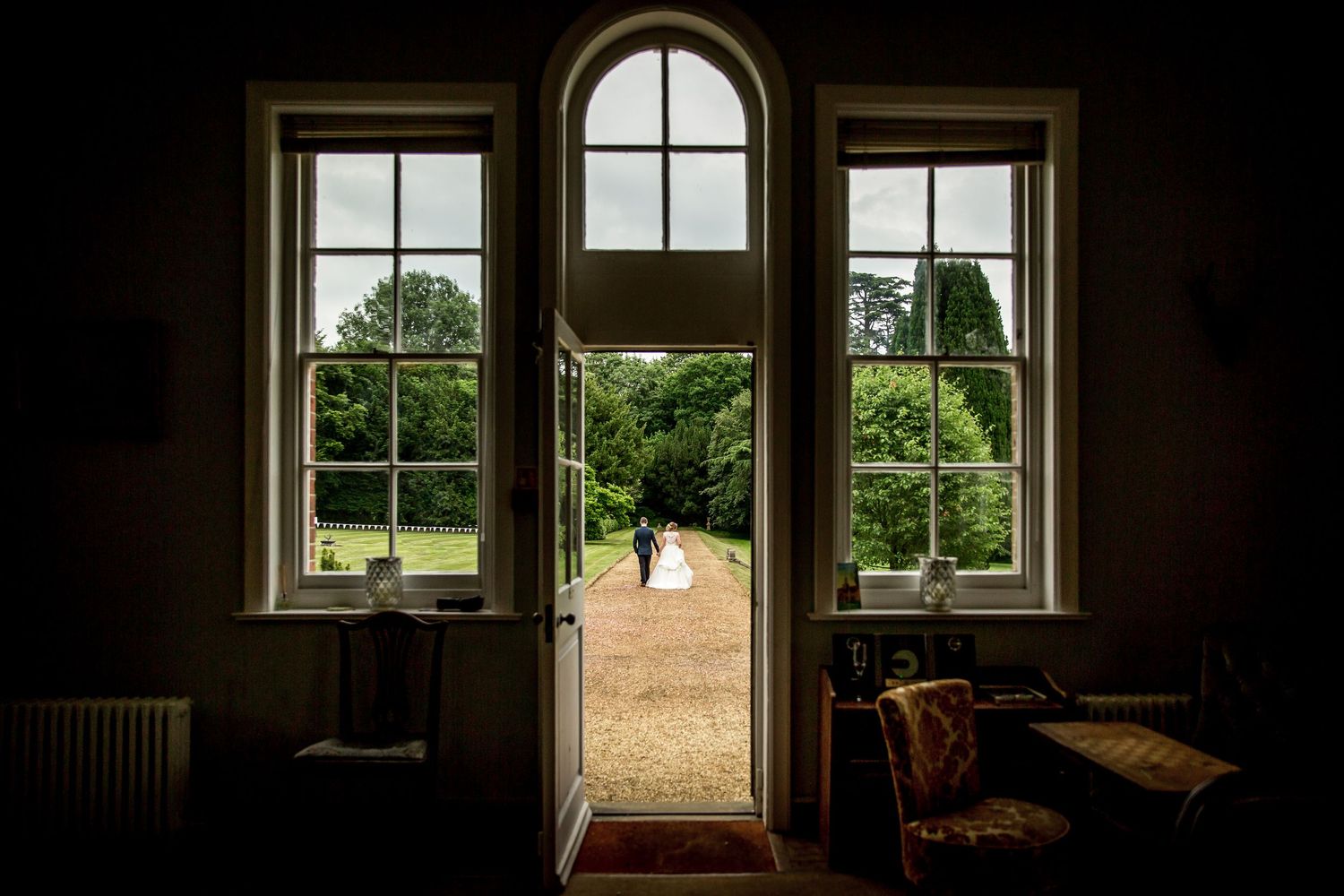 A bride and groom walk along a path in a creative photograph using windows as framing