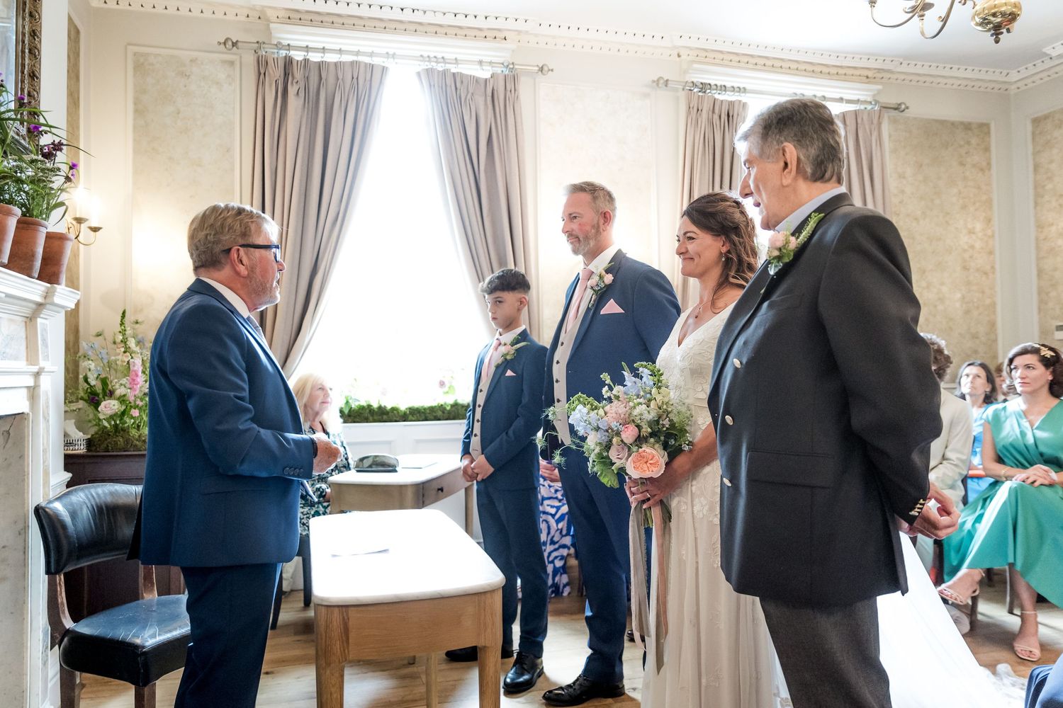 Wedding ceremony taking place in a bright room with elegant curtains and decor.