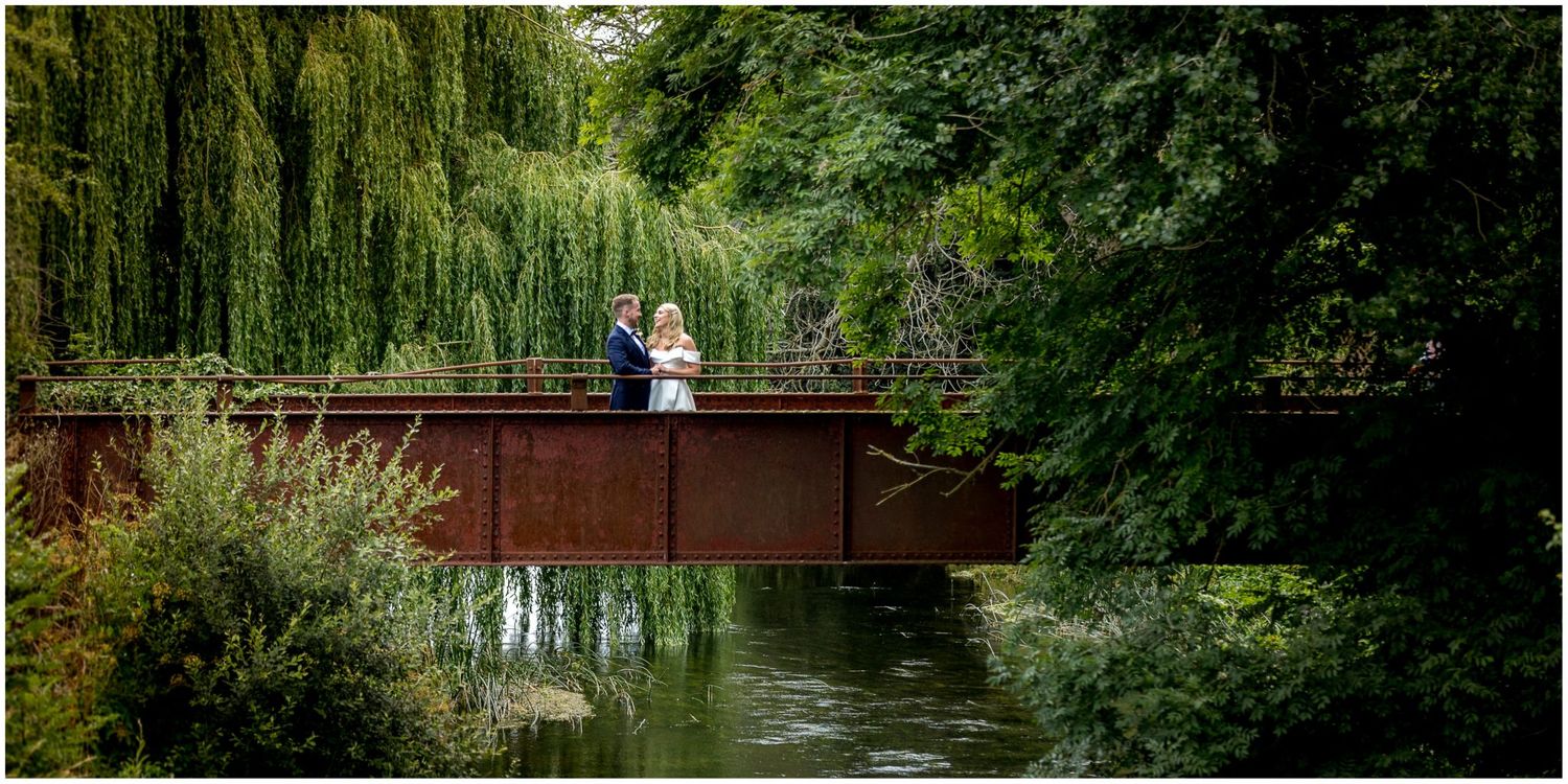 A wedding couple pose on the iconic iron bridge spanning the river behind Sopley Mill, Hampshire wedding venue