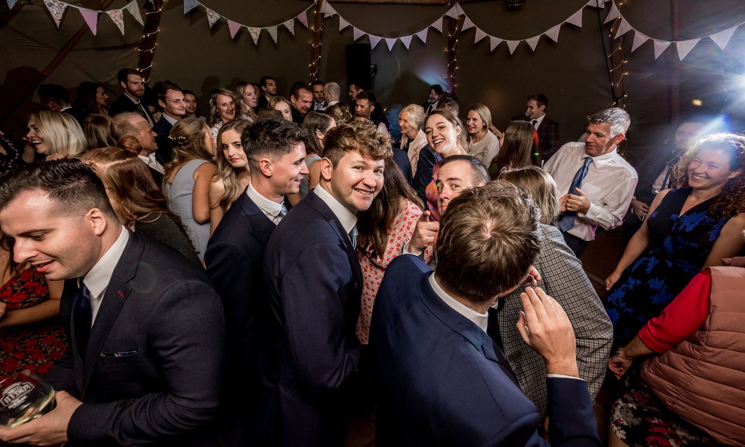 Crowded dance floor at a wedding reception with white bunting decorations hanging from the ceiling.