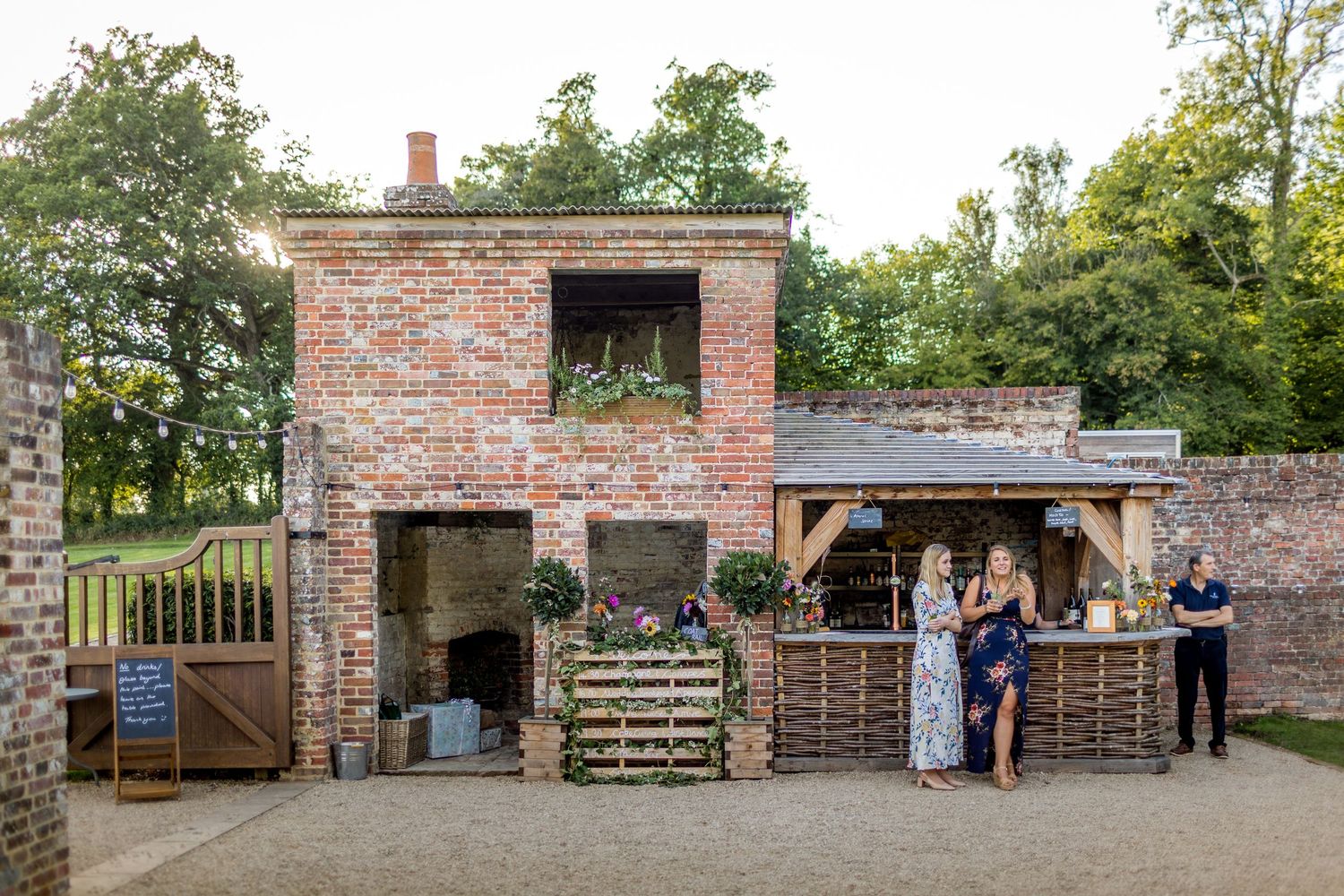 Rustic brick bar setup at an outdoor wedding venue with guests gathering.