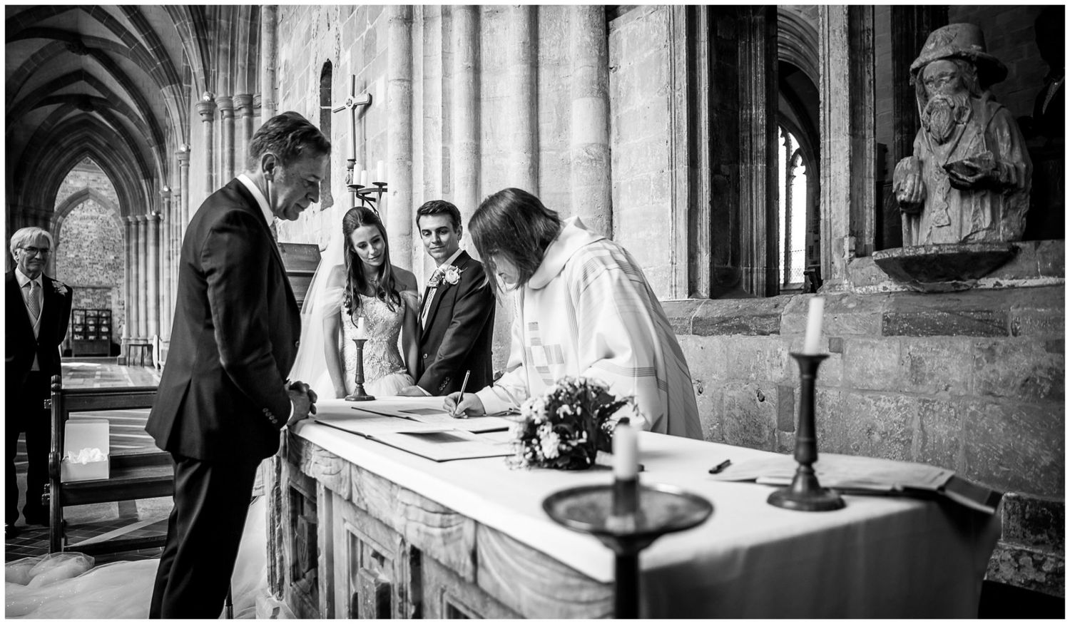 Wedding ceremony preparations in a historic stone church cloister with natural light streaming through windows.
