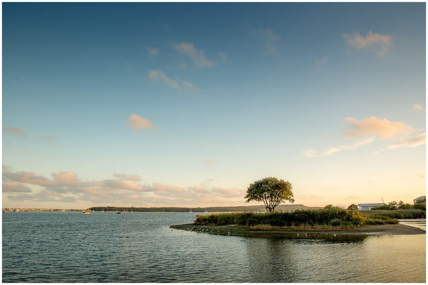 Panoramic coastal landscape at sunset shows calm waters and small islands dotting the tranquil horizon.
