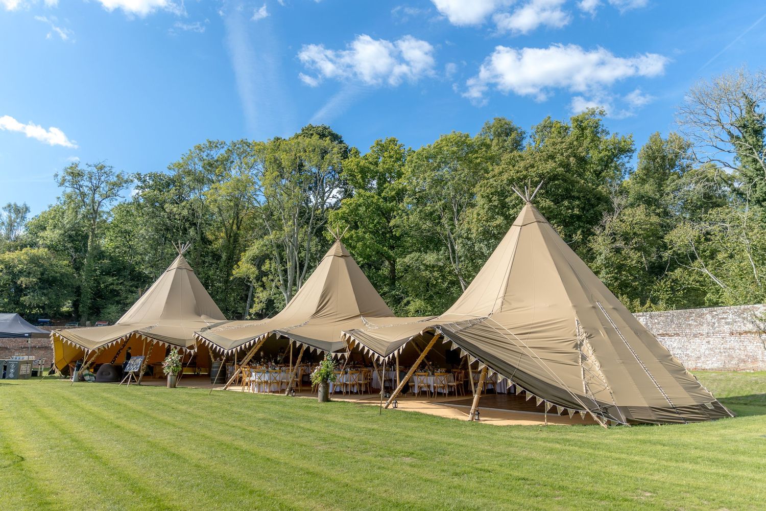 Row of tipi-style event tents arranged on grassy field under summer sky.