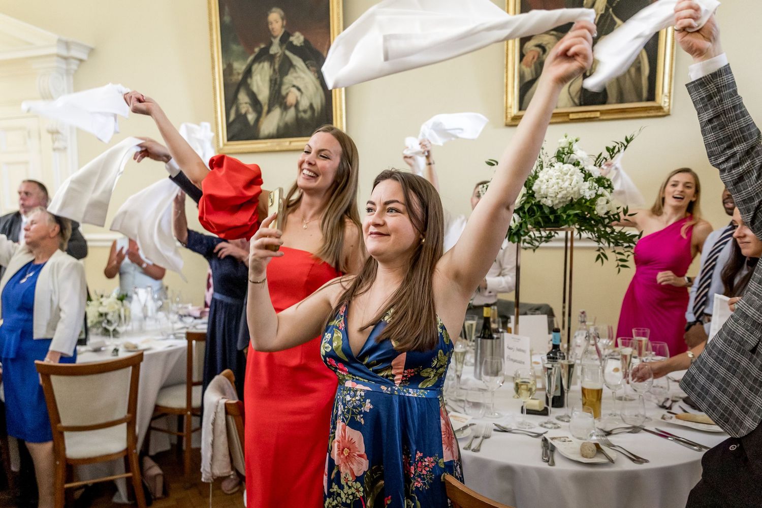 Joyful wedding celebration with guests dancing and raising napkins in elegant ballroom.