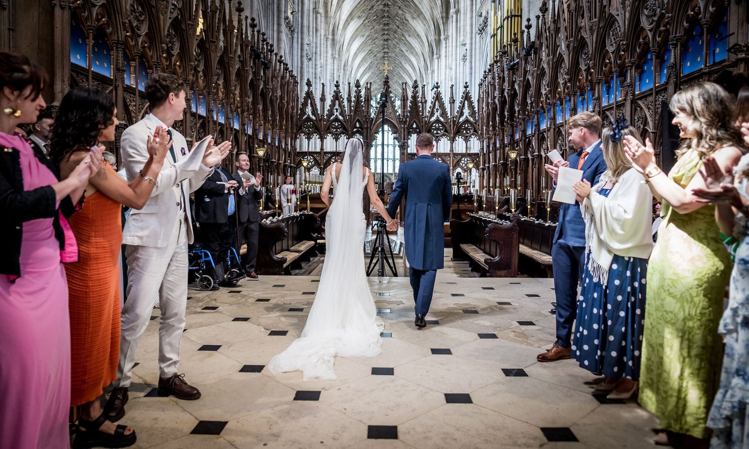 Wedding ceremony taking place in a historic cathedral with checkered floor and ornate decorations.