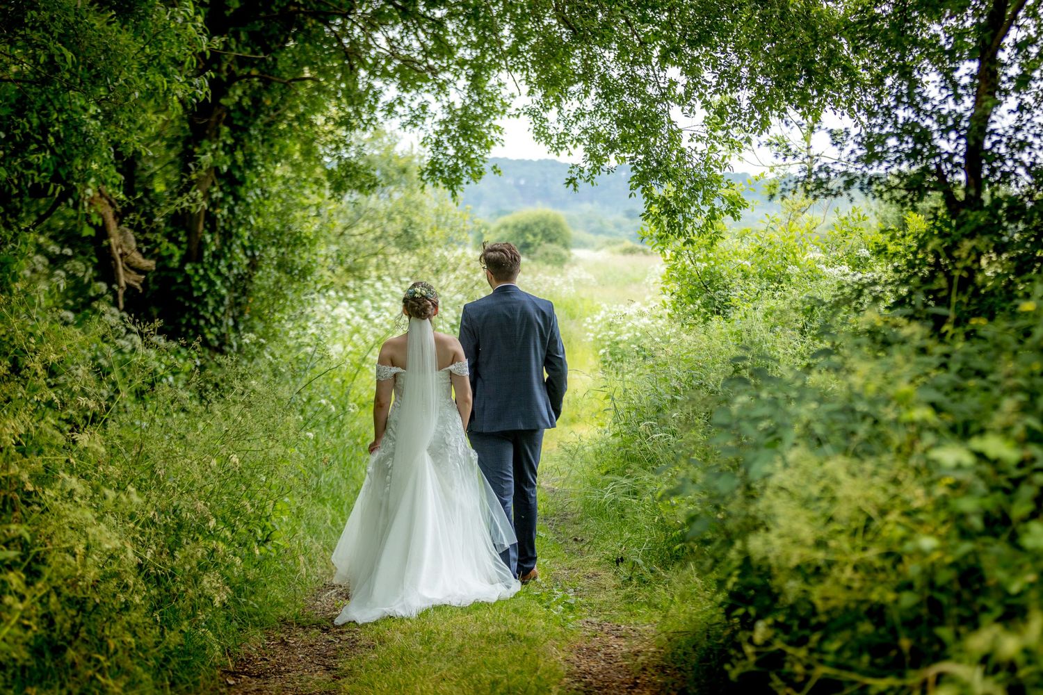 Romantic garden path with natural greenery and white flowers framing a wedding scene.
