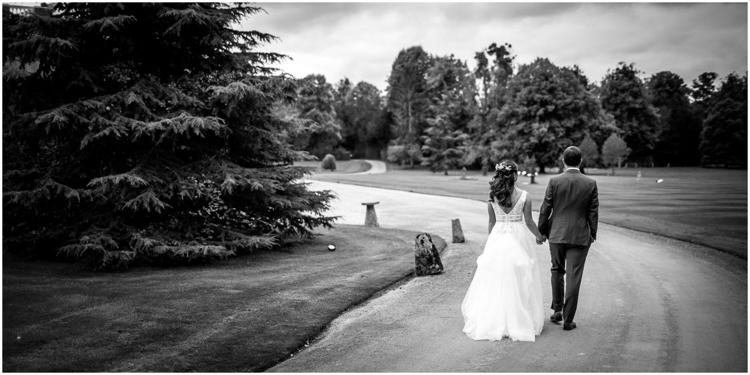 Black and white wedding photo of couple walking along curved garden path.