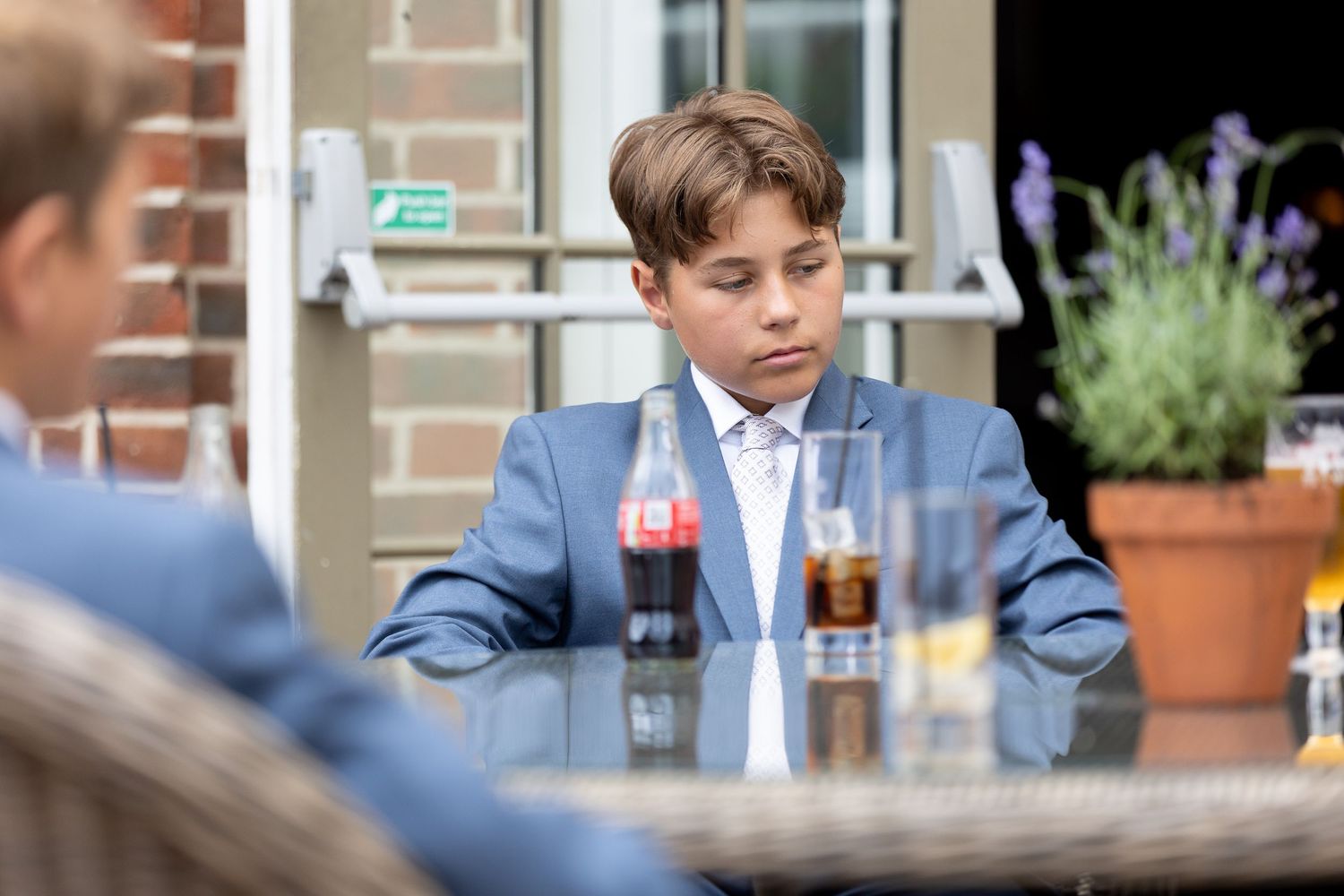 Young person in a blue suit sitting at a table with beverages.